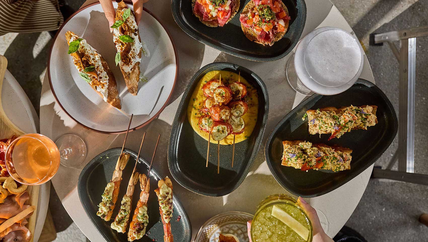Assorted small plates, seafood skewers, crostini, and cocktails shared around a table