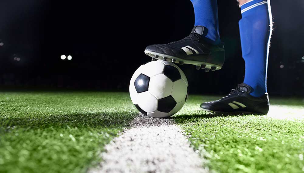 Soccer ball on pitch with player in blue socks