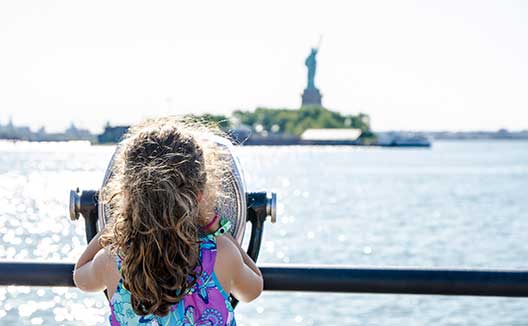 Kid looking at Statue of Liberty through paying binoculars from the Liberty State Park in Jersey city during summer day