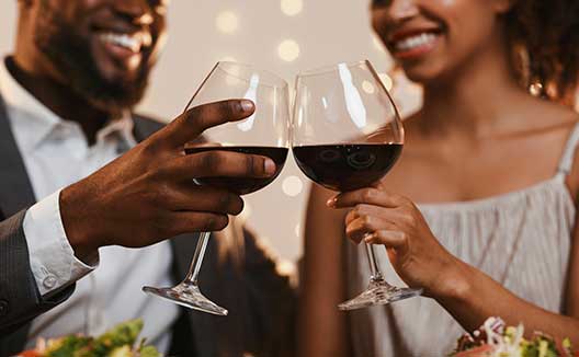 Two people clinking red wine glasses
